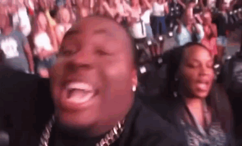 A Man Is Laughing While Sitting In Front Of A Crowd Of People At A Concert . GIF