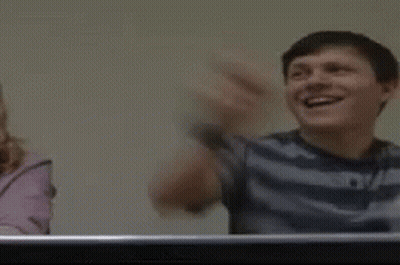 A Man Is Laughing With His Arms In The Air While Sitting At A Table . GIF