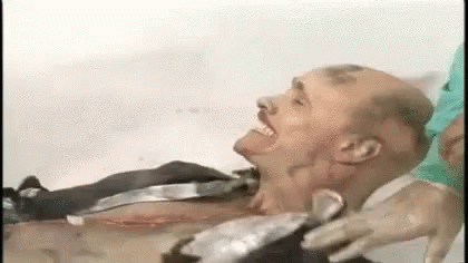 A Man Is Laying In A Bathtub With His Mouth Open While A Nurse Holds His Head . GIF