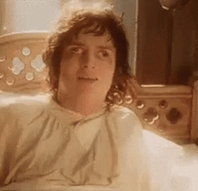 A Man Is Laying In A Bed With A Blanket On His Head And Looking At The Camera . GIF