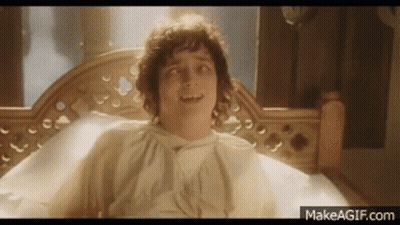 A Man Is Laying In A Bed With A White Shirt On And Smiling . GIF
