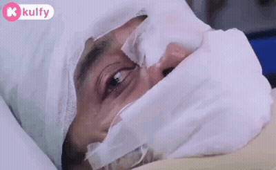 A Man Is Laying In A Hospital Bed With A Bandage On His Head And Face . GIF