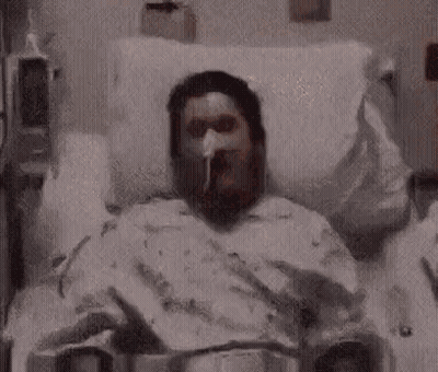 A Man Is Laying In A Hospital Bed With An Oxygen Mask On . GIF