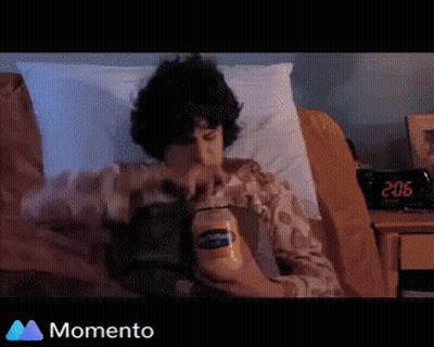 A Man Is Laying In Bed Holding A Bottle Of Peanut Butter GIF