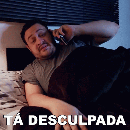 A Man Is Laying In Bed Talking On A Cell Phone With The Caption Ta Desculpada Above Him GIF