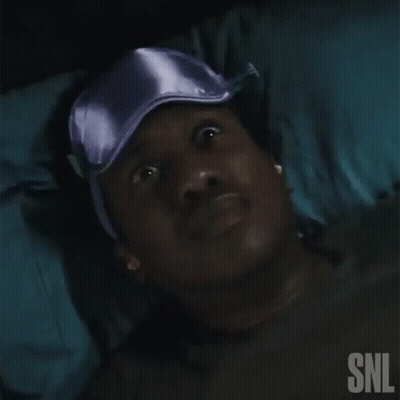 A Man Is Laying In Bed Wearing A Purple Sleep Mask . GIF