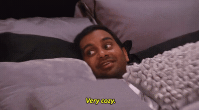 A Man Is Laying In Bed With A Blanket And A Pillow . GIF