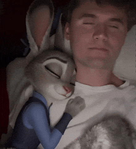 A Man Is Laying In Bed With A Stuffed Animal Rabbit On His Chest GIF