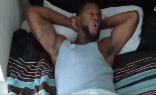 A Man Is Laying In Bed With His Arms Outstretched . GIF