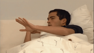 A Man Is Laying In Bed With His Hand Out GIF