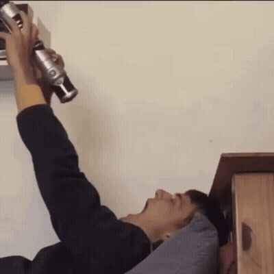 A Man Is Laying On A Bed Holding A Green Lightsaber GIF