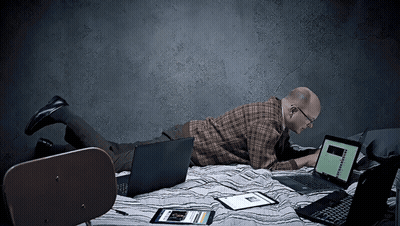 A Man Is Laying On A Bed Using A Laptop And A Tablet GIF