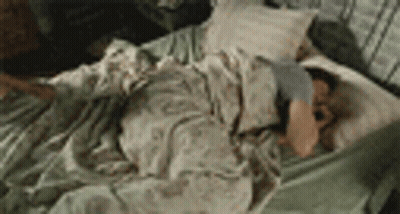 A Man Is Laying On A Bed With A Blanket And Pillow . GIF