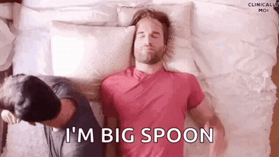 A Man Is Laying On A Bed With A Pillow On His Head And Another Man Is Standing Behind Him . GIF