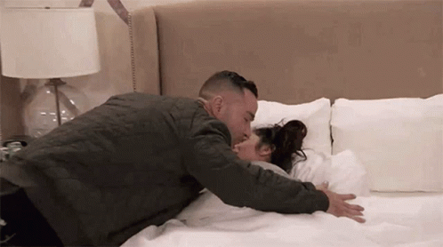 A Man Is Laying On A Bed With A Woman And Kissing Her . GIF