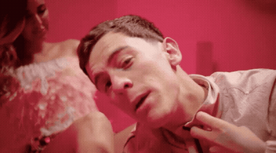 A Man Is Laying On A Bed With A Woman In A Pink Dress Behind Him GIF