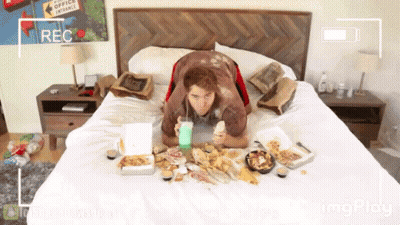 A Man Is Laying On A Bed With Boxes Of Food And A Sign That Says Office Entrance On The Wall Behind Him GIF