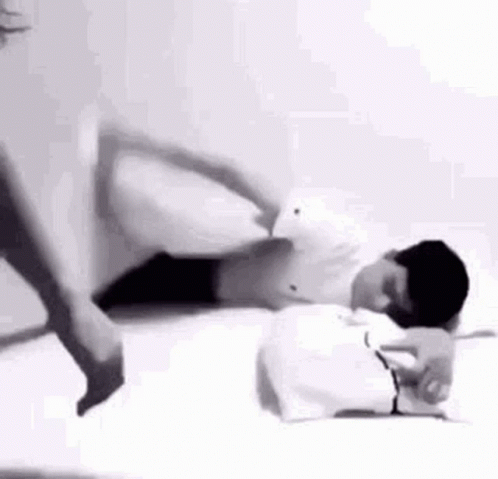 A Man Is Laying On A Bed With His Legs Crossed And A Person Is Standing Next To Him . GIF
