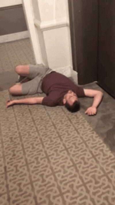 A Man Is Laying On A Carpet In A Hallway . GIF
