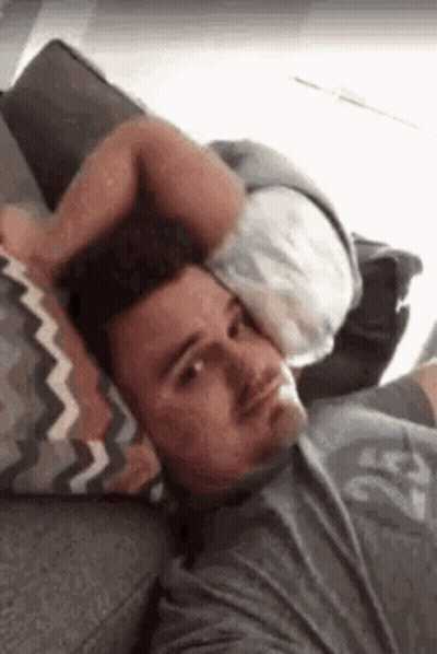 A Man Is Laying On A Couch Holding A Pillow Over His Head . GIF