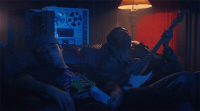 A Man Is Laying On A Couch While Another Man Holds A Guitar GIF