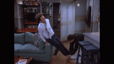 A Man Is Laying On A Couch While Another Man Holds His Legs Up In The Air . GIF