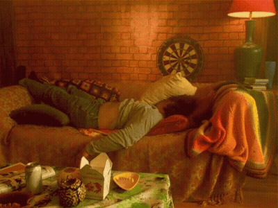 A Man Is Laying On A Couch With A Dart Board In The Background GIF
