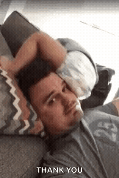 A Man Is Laying On A Couch With A Pillow On His Head And A Baby On His Head . GIF