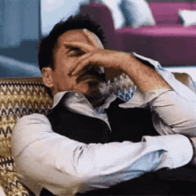 A Man Is Laying On A Couch With His Hand On His Forehead . GIF
