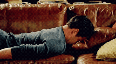 A Man Is Laying On A Leather Couch With His Head On A Pillow . GIF