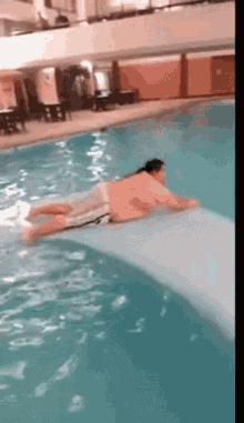 A Man Is Laying On A Slide In A Swimming Pool GIF