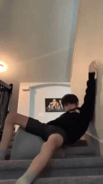 A Man Is Laying On A Staircase With His Legs Crossed And A Picture Of A Man On The Wall Behind Him . GIF