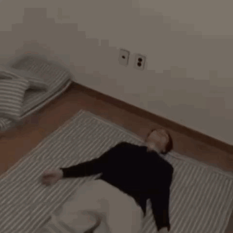A Man Is Laying On A Striped Blanket On The Floor GIF