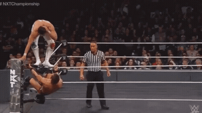 A Man Is Laying On His Back In A Wrestling Ring While Another Man Kicks Him . GIF