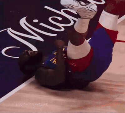 A Man Is Laying On His Back On A Basketball Court In Front Of A Michigan Sign GIF