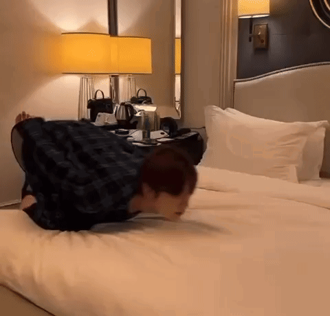 A Man Is Laying On His Back On A Bed In A Hotel Room GIF