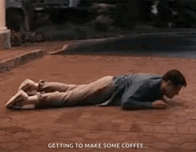 A Man Is Laying On His Stomach On A Brick Sidewalk Drinking Coffee . GIF