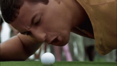 A Man Is Laying On His Stomach On A Golf Course Looking At A Golf Ball . GIF