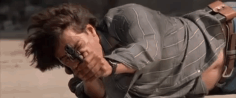 A Man Is Laying On The Ground Holding A Gun And Pointing It At The Camera . GIF