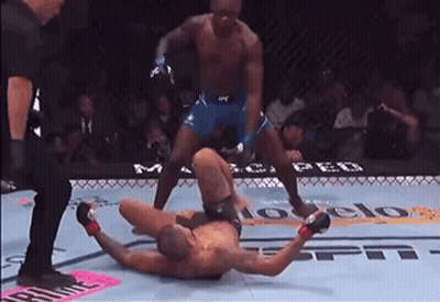 A Man Is Laying On The Ground In A Boxing Ring While A Referee Watches . GIF