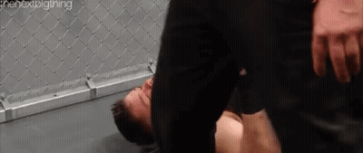 A Man Is Laying On The Ground In A Boxing Ring While Another Man Is Standing Over Him . GIF