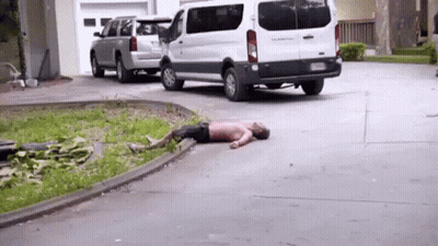 A Man Is Laying On The Ground In A Driveway Next To A White Van . GIF