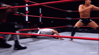 A Man Is Laying On The Ground In A Wrestling Ring While Another Man Is Standing In The Ring . GIF