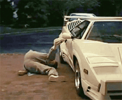 A Man Is Laying On The Ground In Front Of A White Car GIF