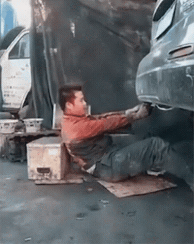 A Man Is Laying On The Ground Working On A Car 'S Exhaust Pipe . GIF