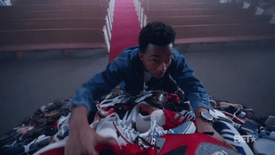 A Man Is Laying On Top Of A Pile Of Shoes With A Bet Logo In The Background GIF