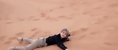 A Man Is Laying On Top Of A Sand Dune In The Desert . GIF