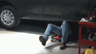 A Man Is Laying Under A Car In A Garage With His Head Underneath The Car GIF