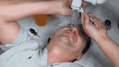 A Man Is Laying Under A Sink With Water Coming Out Of The Pipes GIF