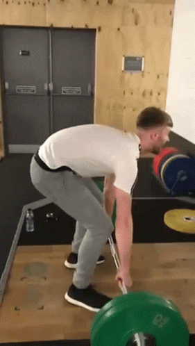 A Man Is Lifting A Barbell In A Gym . GIF